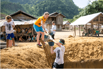 Students working on a community service project in a remote village in Thailand, surrounded by mountains and simple rural structures. Students working on a community service project in a remote village in Thailand, surrounded by mountains and simple rural structures.